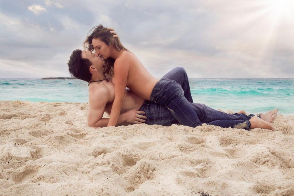 couple laying on top of each other topless and wearing jeans on the beach