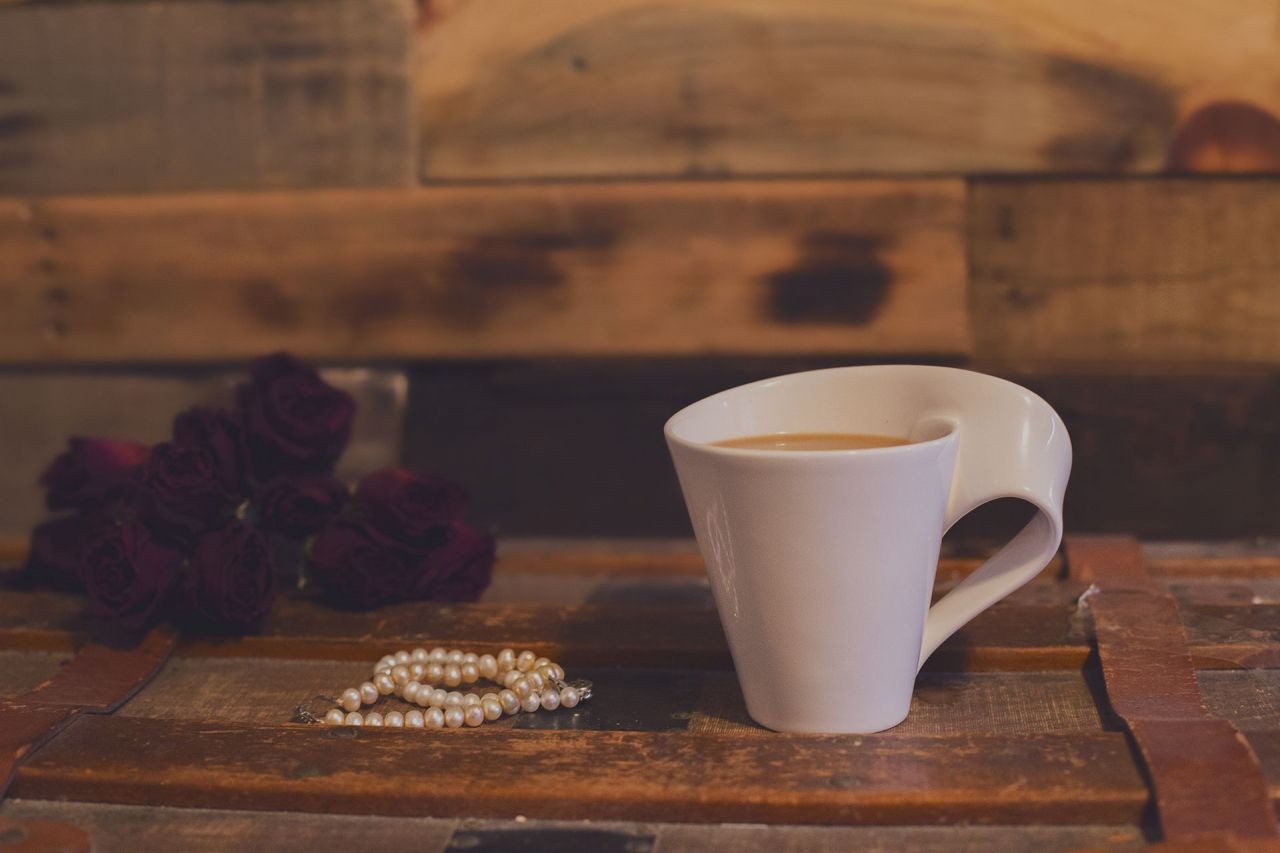 A cup of hot chocolate on a wooden crate with a pearl necklace next to the cup